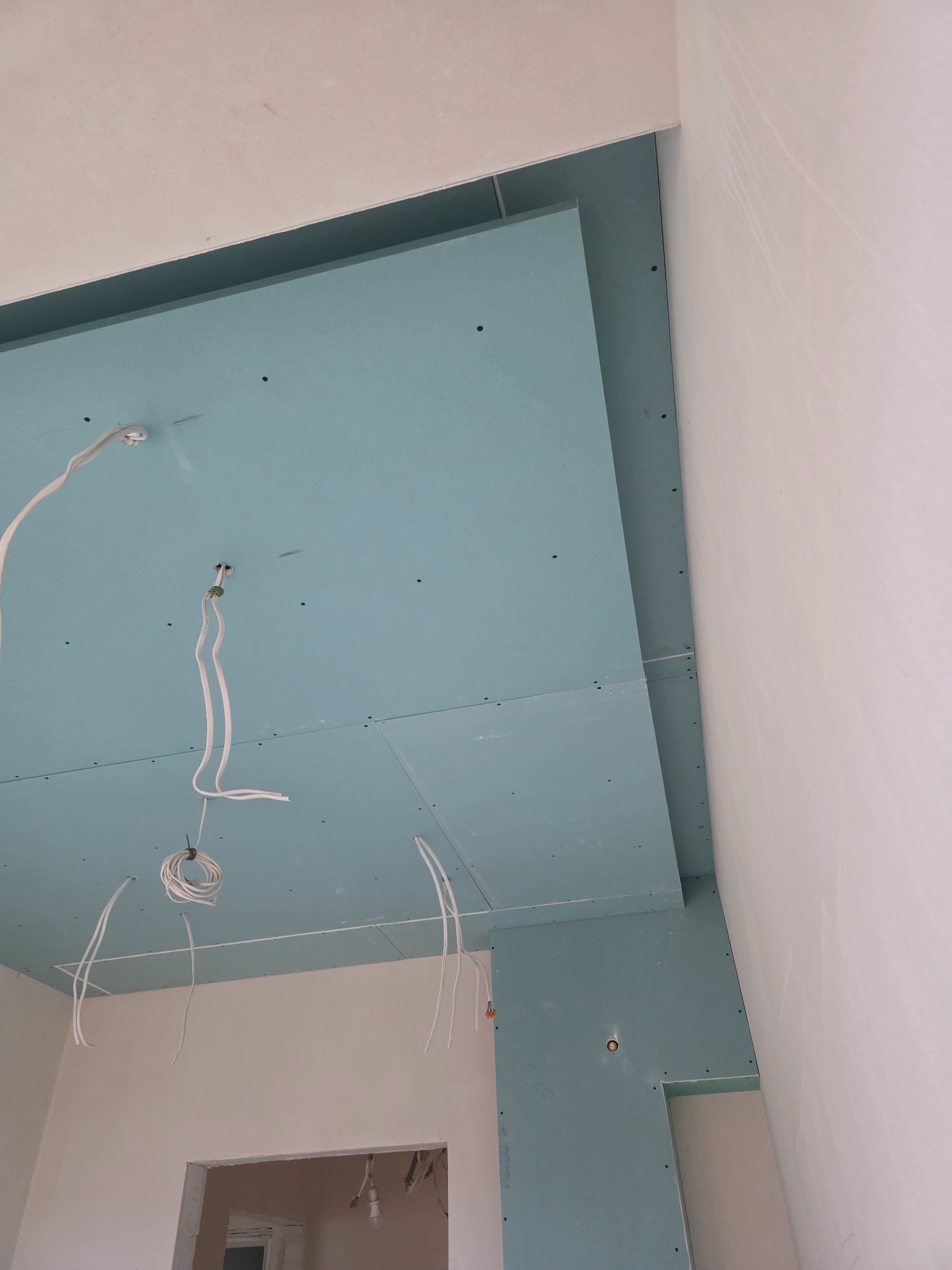 Niebieskie płyty kartonowo-gipsowe na suficie, widoczne kable elektryczne. Etap prac wykończeniowych w pomieszczeniu z surowymi ścianami.