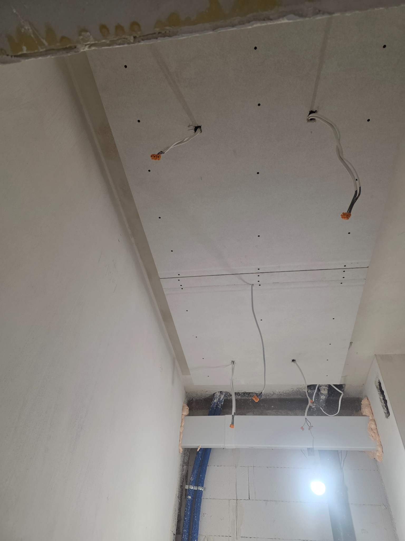 Sufit podwieszany z płyt gipsowo-kartonowych w trakcie montażu, widoczne przewody elektryczne i profile. Ściany w surowym stanie, przygotowane do dalszych prac.