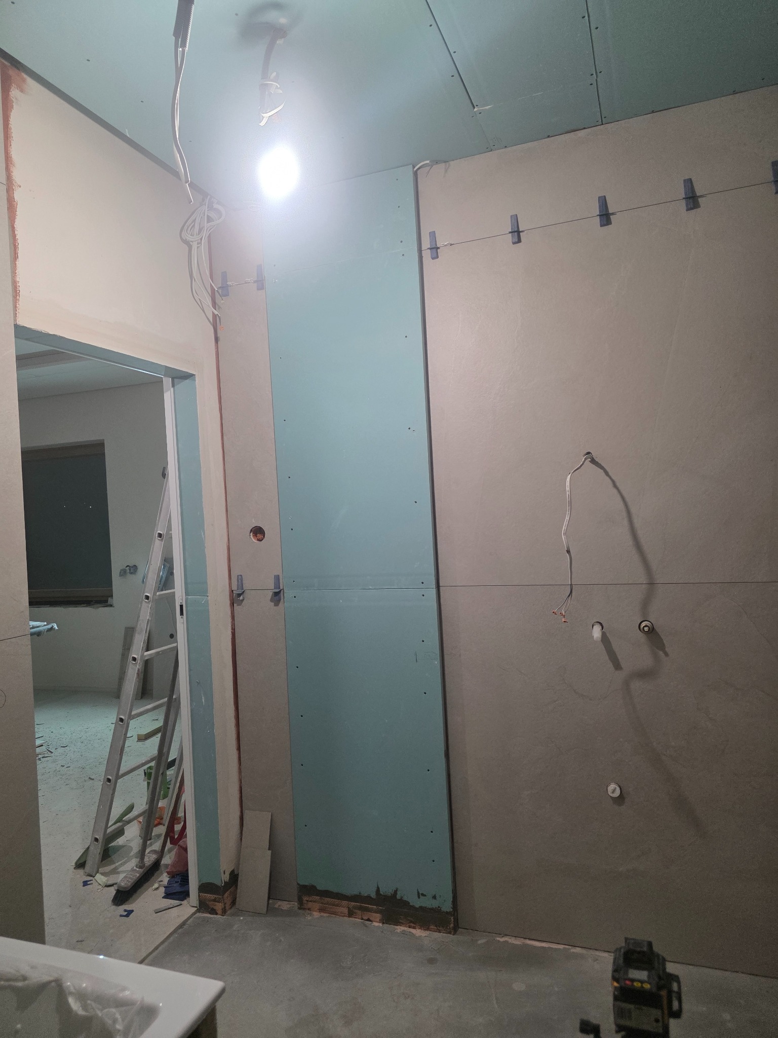Montaż płyt gipsowo-kartonowych w łazience, widoczne profile, przewody elektryczne i poziomica laserowa. Etap prac wykończeniowych, surowy stan.