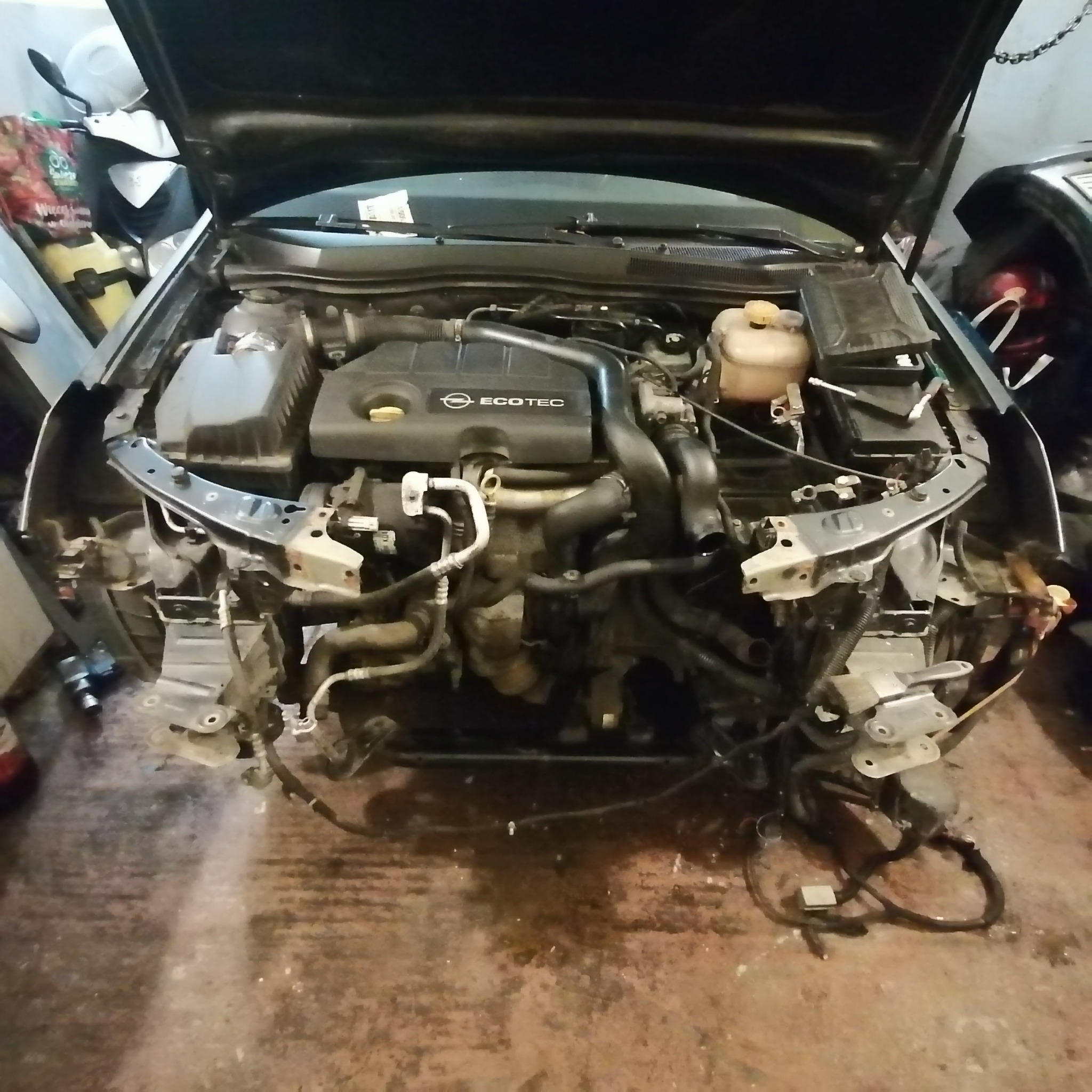 Widok na silnik samochodu Opel Astra z otwartą maską, zdemontowany przód pojazdu, widoczne elementy zawieszenia i instalacji elektrycznej, silnik ECOTEC.