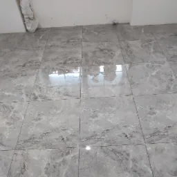 Ułożona szara, marmurkowa podłoga z płytek ceramicznych w pustym pomieszczeniu z białymi ścianami, widoczne pozostałości po zabezpieczeniu narożnika ściany.