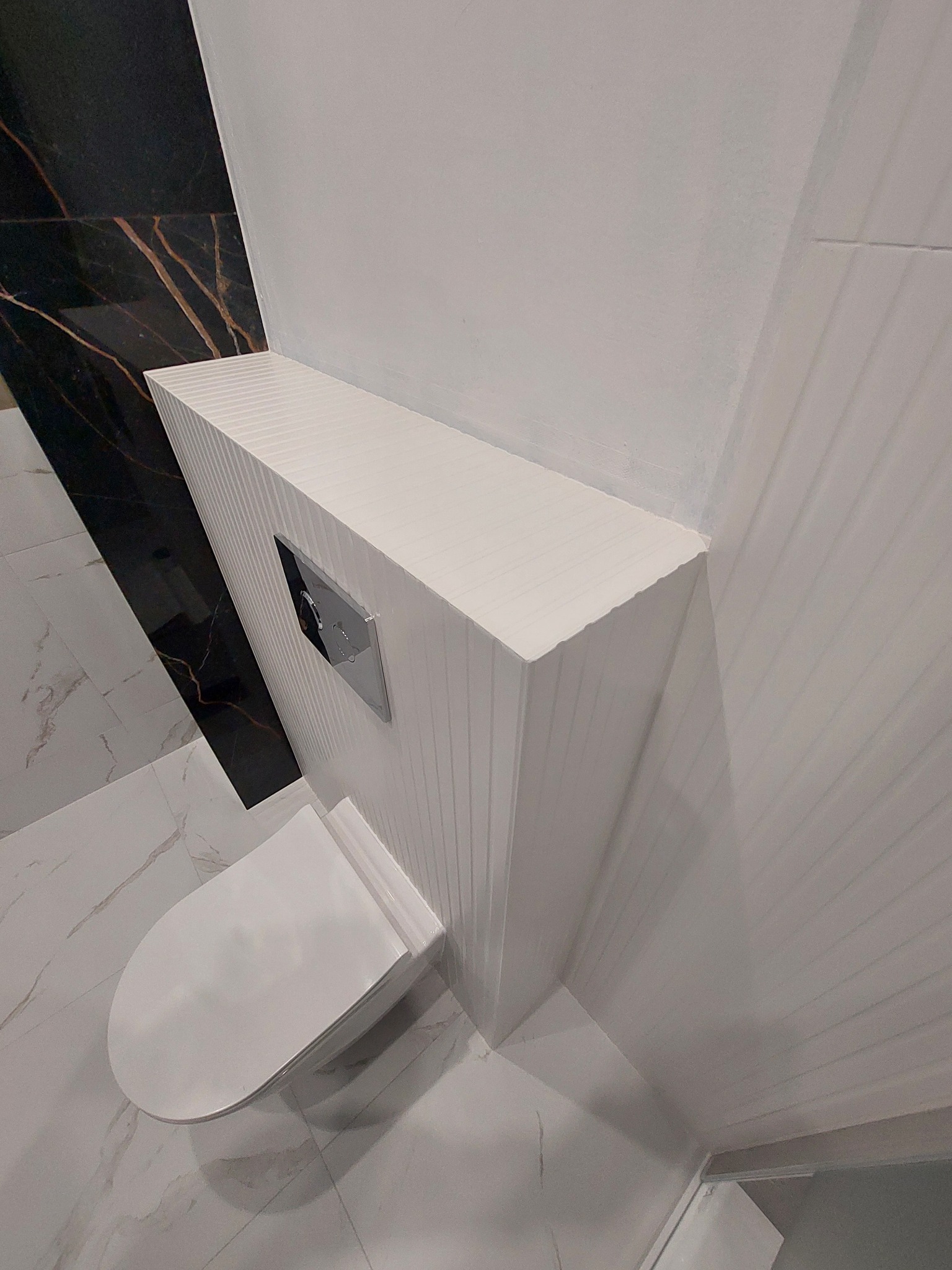 Nowoczesna toaleta podwieszana z białym, ryflowanym stelażem i czarną płytą z marmurowym wzorem w wykończonej łazience.