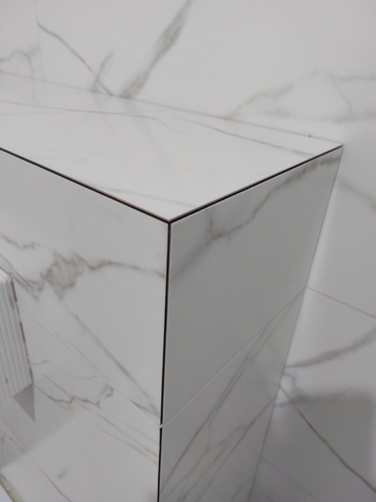 Detal narożnika obudowy w łazience z płytek imitujących marmur, z czarną fugą. Precyzyjne cięcie i układanie płytek, gładka powierzchnia, minimalistyczny design.