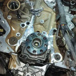 Widok z góry na rozmontowany silnik samochodowy z widocznymi elementami metalowymi, przewodami i śladami oleju.