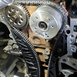 Service Point - Silnik samochodowy w trakcie naprawy, widoczny rozrząd z łańcuchem, koła zębate i napinacz łańcucha, zbliżenie na mechanizm.