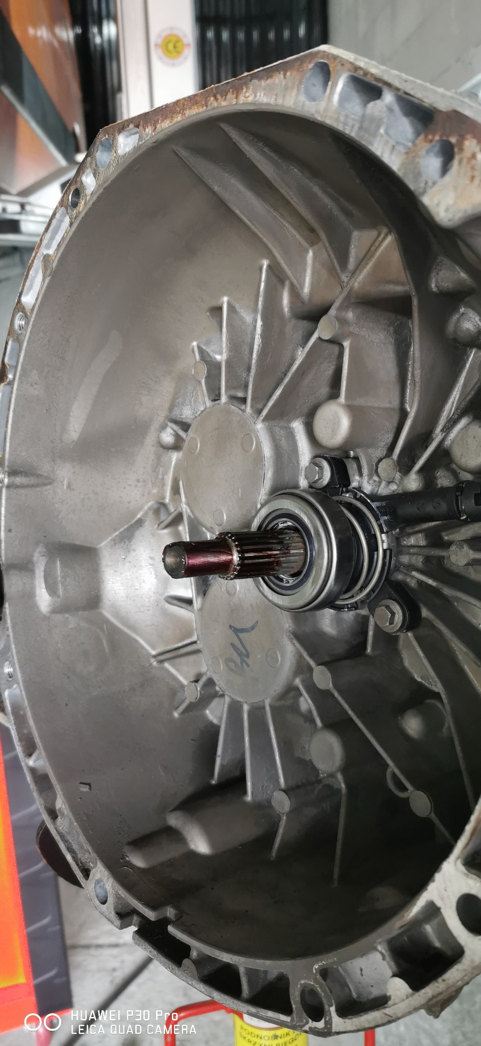 Szczegółowe ujęcie aluminiowej obudowy skrzyni biegów z widocznym łożyskiem oporowym sprzęgła i wałkiem, oznaczona szarym markerem, widoczne ślady korozji na obrzeżach.