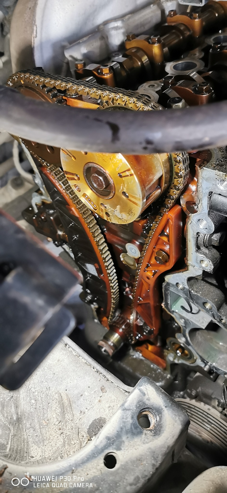 Olejem pokryty łańcuch rozrządu silnika samochodowego podczas naprawy, widoczne koła zębate i elementy głowicy cylindrów.