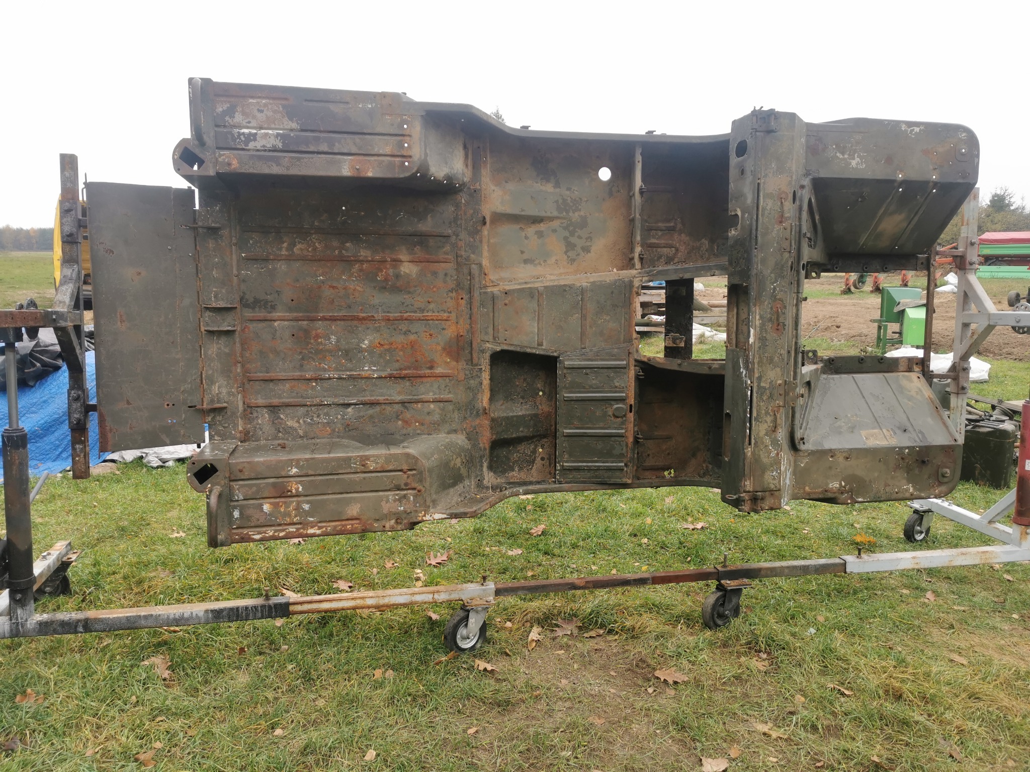 Częściowo skorodowana karoseria pojazdu, prawdopodobnie zabytkowego, zawieszona na metalowym stelażu z kółkami w Kolbuszowej, przygotowana do renowacji.