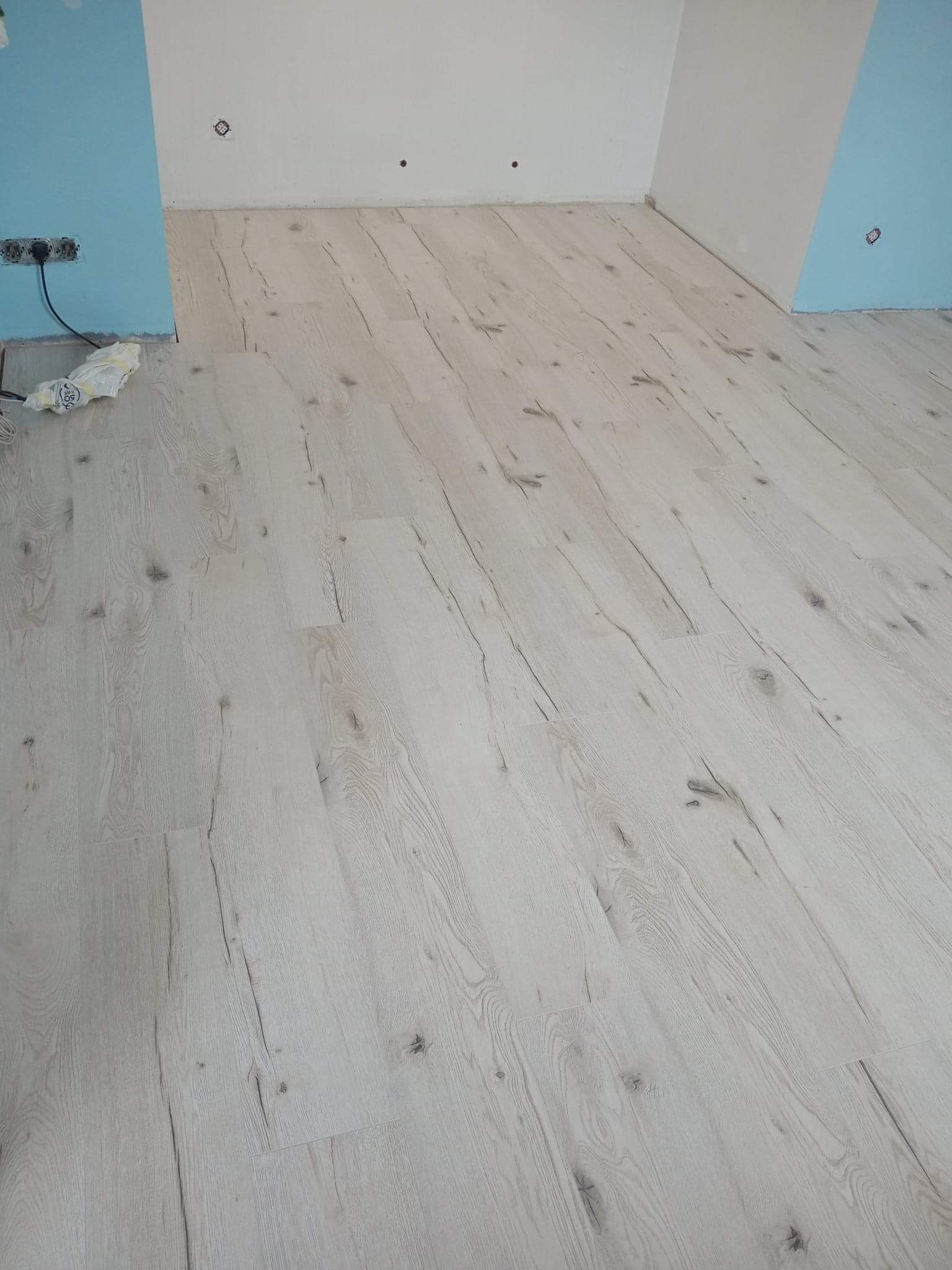 Ułożona podłoga z paneli imitujących jasne drewno, widoczne puszki elektryczne na ścianach w trakcie remontu.