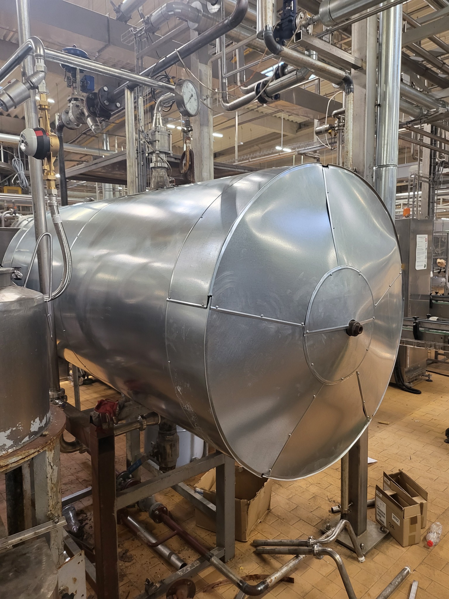 Duży, poziomy, metalowy zbiornik w przemysłowym otoczeniu z rurami i konstrukcjami wsporczymi, widoczne elementy podłączeń i manometry.