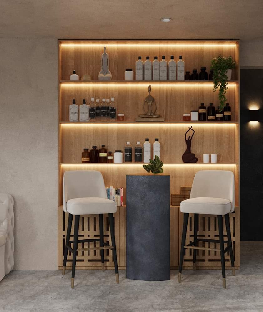 Jasne wnętrze z drewnianą półką podświetloną LED z dekoracyjnymi przedmiotami, krzesła barowe z beżową tapicerką i czarnymi nogami, szary postument z rośliną.