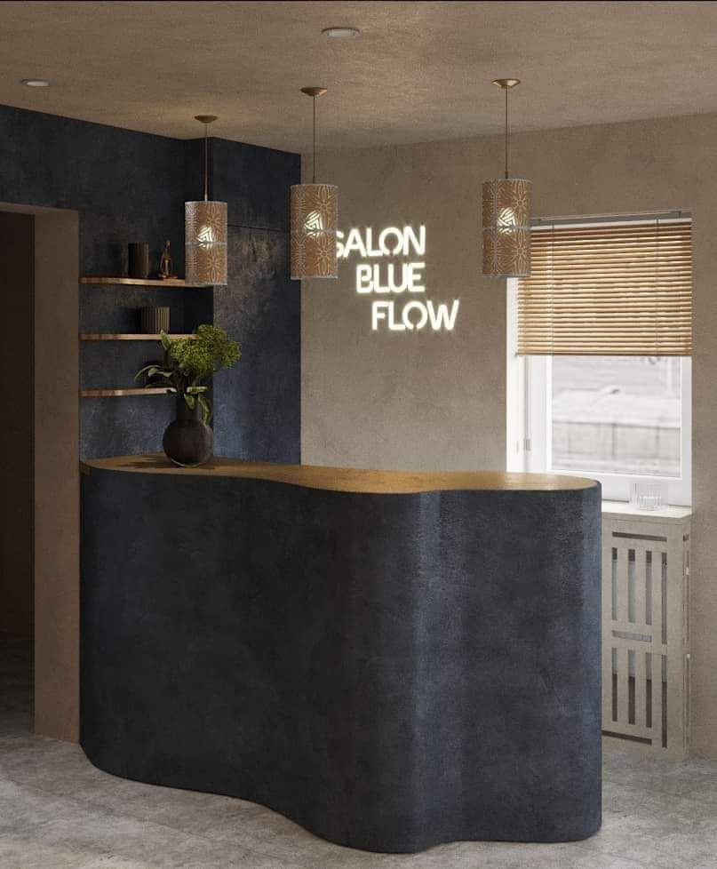 Recepcja salonu z ciemnym, falistym blatem, oświetlona trzema wiszącymi lampami z ażurowymi abażurami i neonem 'SALON BLUE FLOW' na ścianie.