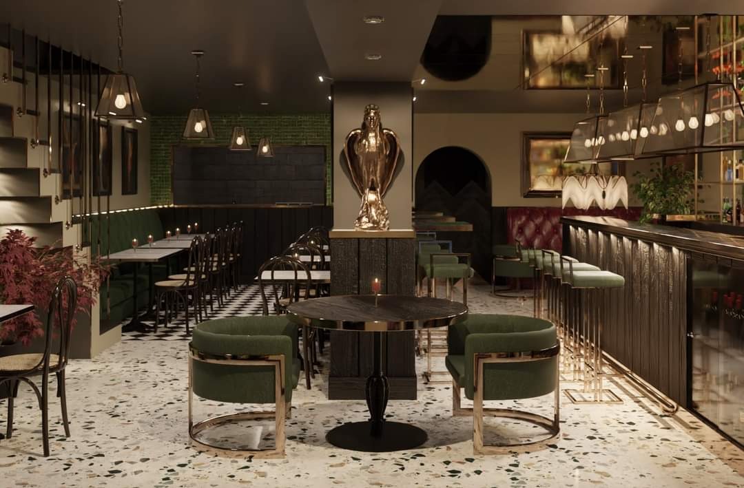 Eleganckie wnętrze restauracji z zielonymi akcentami: okrągły stolik z dwoma fotelami, bar z wysokimi stołkami, dekoracyjna rzeźba anioła, podłoga lastryko, oświetlenie wiszące.