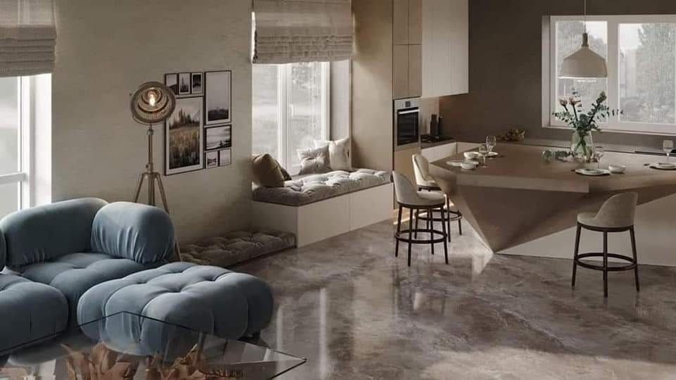 Nowoczesne wnętrze z otwartą przestrzenią: szary, modułowy narożnik, okno z siedziskiem i poduszkami, lampa stojąca na trójnogu, aneks kuchenny z wyspą i hokerami, marmurowa podłoga.