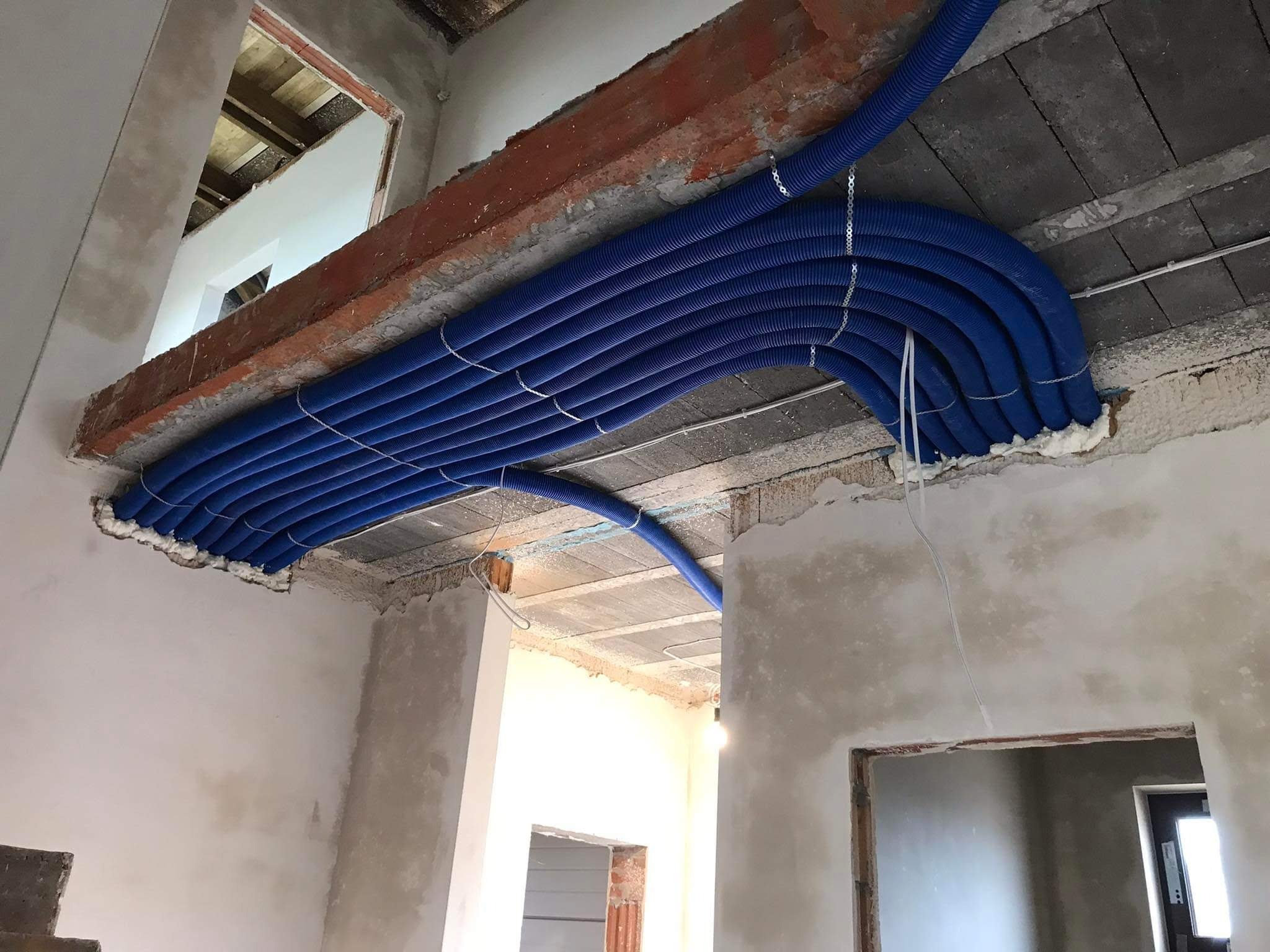 Równolegle ułożone, niebieskie rury wentylacyjne pod sufitem w surowym wnętrzu, zabezpieczone pianką montażową i metalowymi zawieszkami.