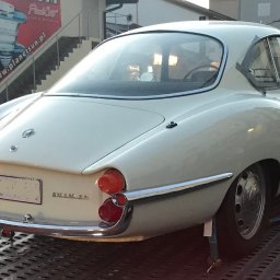 Car Point Adrian Krzysztofik - Biała Alfa Romeo Giulia SS z 1963 roku na lawecie, widok z tyłu, z chromowanymi detalami i okrągłymi światłami. Klasyczny włoski design.