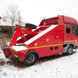 Car Point Adrian Krzysztofik - Czerwona laweta pomocy drogowej Superior na śniegu, z wysuniętym ramieniem holowniczym. Widoczny budynek w tle i logo firmy na pojeździe.