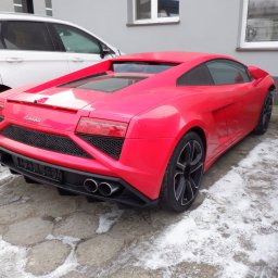 Car Point Adrian Krzysztofik - Czerwone Lamborghini Gallardo z tyłu, zaparkowane na betonowym podłożu z resztkami śniegu, obok innych aut. Widoczne detale: czarne felgi, podwójny wydech.