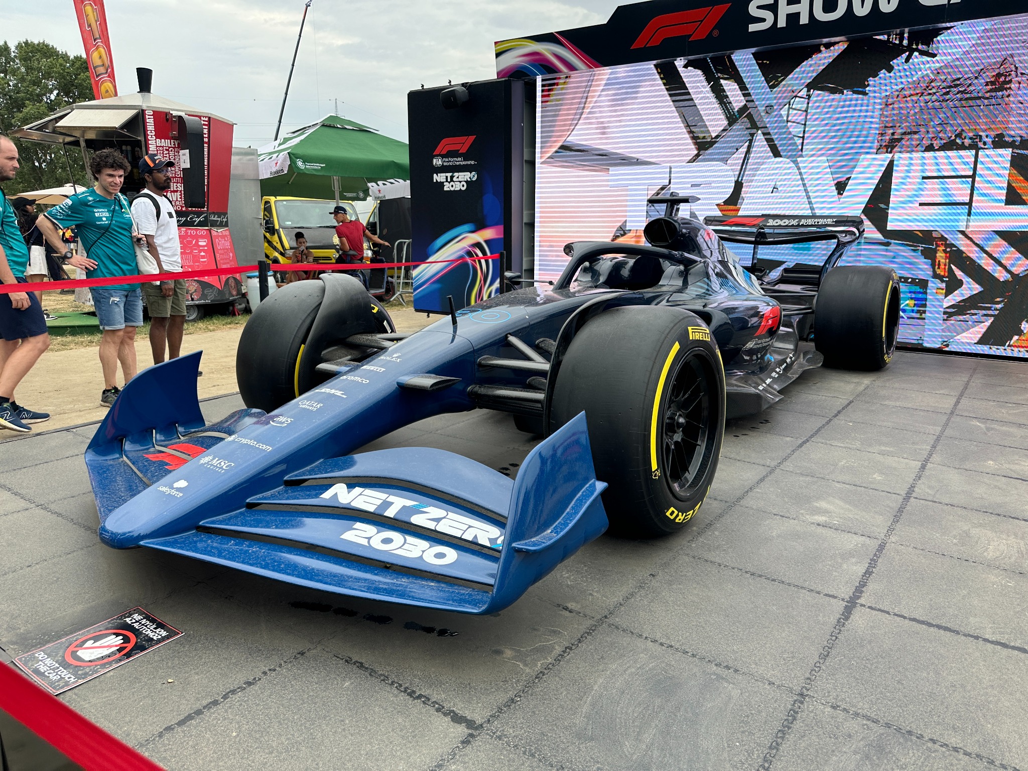 Niebieski bolid Formuły 1 'Net Zero 2030' na ekspozycji plenerowej, z widocznymi logotypami sponsorów i napisem '100% Sustainable Fuel' na tylnym skrzydle.