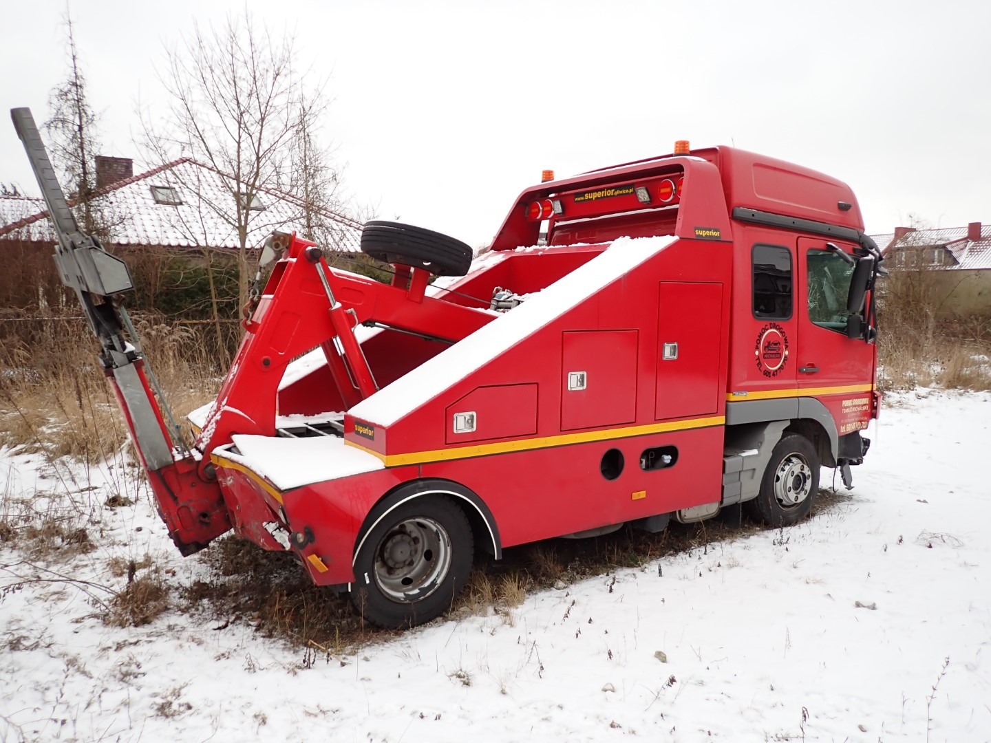 Czerwona laweta pomocy drogowej Superior na śniegu, z wysuniętym ramieniem holowniczym. Widoczny budynek w tle i logo firmy na pojeździe.