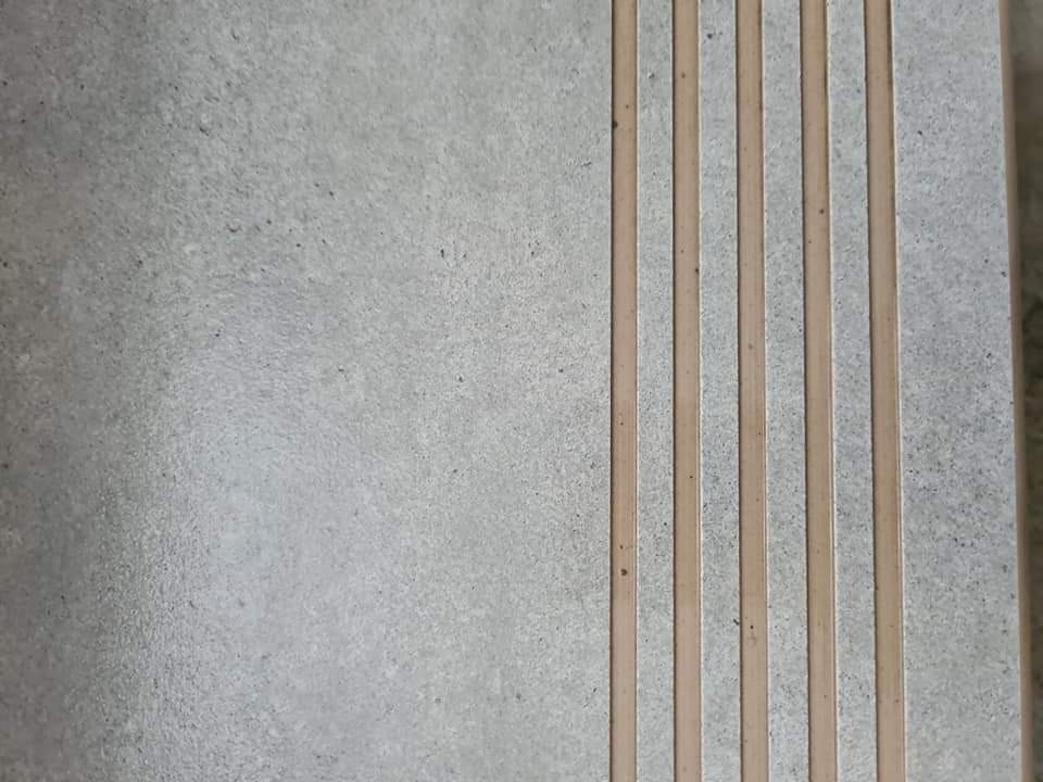 Szara płytka podłogowa z czterema jasnymi, podłużnymi wstawkami antypoślizgowymi.