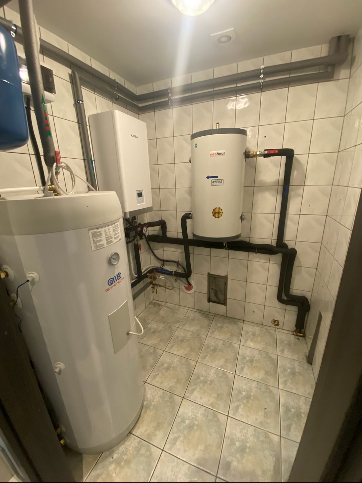 Instalacja z trzema zbiornikami, w tym jednym marki KAISAI, z rurami w pomieszczeniu wyłożonymi kafelkami.
