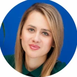 Portret kobiety o jasnych włosach i zielonych oczach, ubranej w zieloną koszulę na tle niebieskiego koła. Widoczny fragment rośliny po lewej stronie.