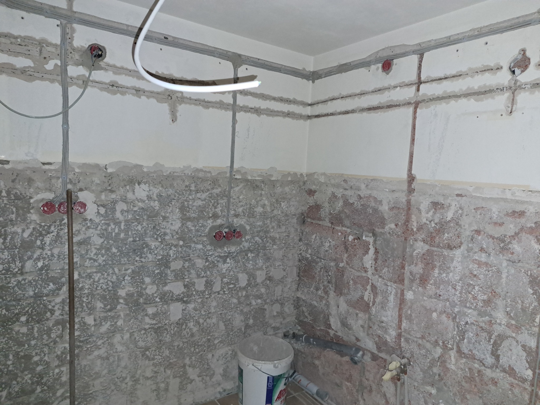 Wnętrze w trakcie prac elektrycznych: widoczne kable w peszlach przymocowane do sufitu i ścian, wyfrezowane bruzdy pod przewody, puszki elektryczne w ścianach, surowe ściany częściowo otynkowane...