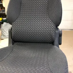 Szare, tekstylne siedzenie samochodowe z wzorem w romby, widoczne z przodu w warsztacie.