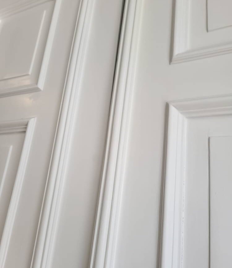 Fragment białej, lakierowanej zabudowy meblowej z frezowanymi detalami, widok z bliska.