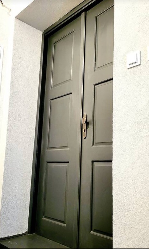 Dwuskrzydłowe, grafitowe drzwi z panelami, złota klamka, biała ściana z przełącznikiem światła, widok z dołu.