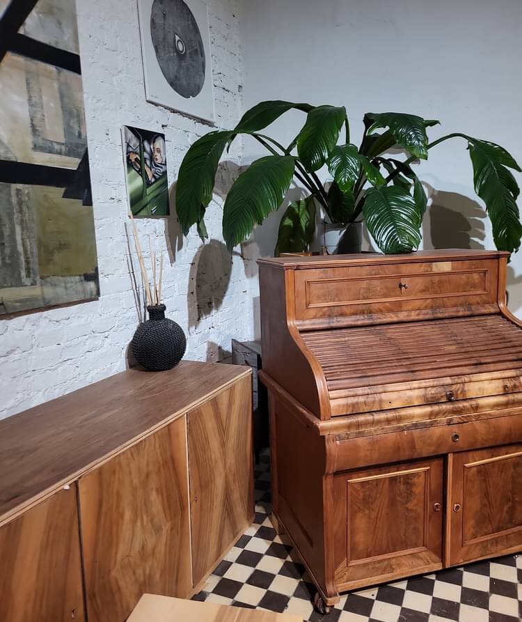Antyczne biurko z roletą i szafka z forniru orzechowego na tle białej ceglanej ściany z obrazami, uzupełnione rośliną doniczkową i zapachem do wnętrz.