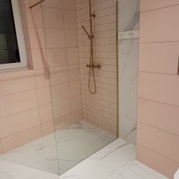 KAF-REM Wykończenia Wnętrz - Nowoczesna łazienka z różowymi płytkami cegiełkami, marmurową ścianą, kabiną prysznicową typu walk-in ze złotą armaturą i białymi marmurowymi płytkami podłogowymi.