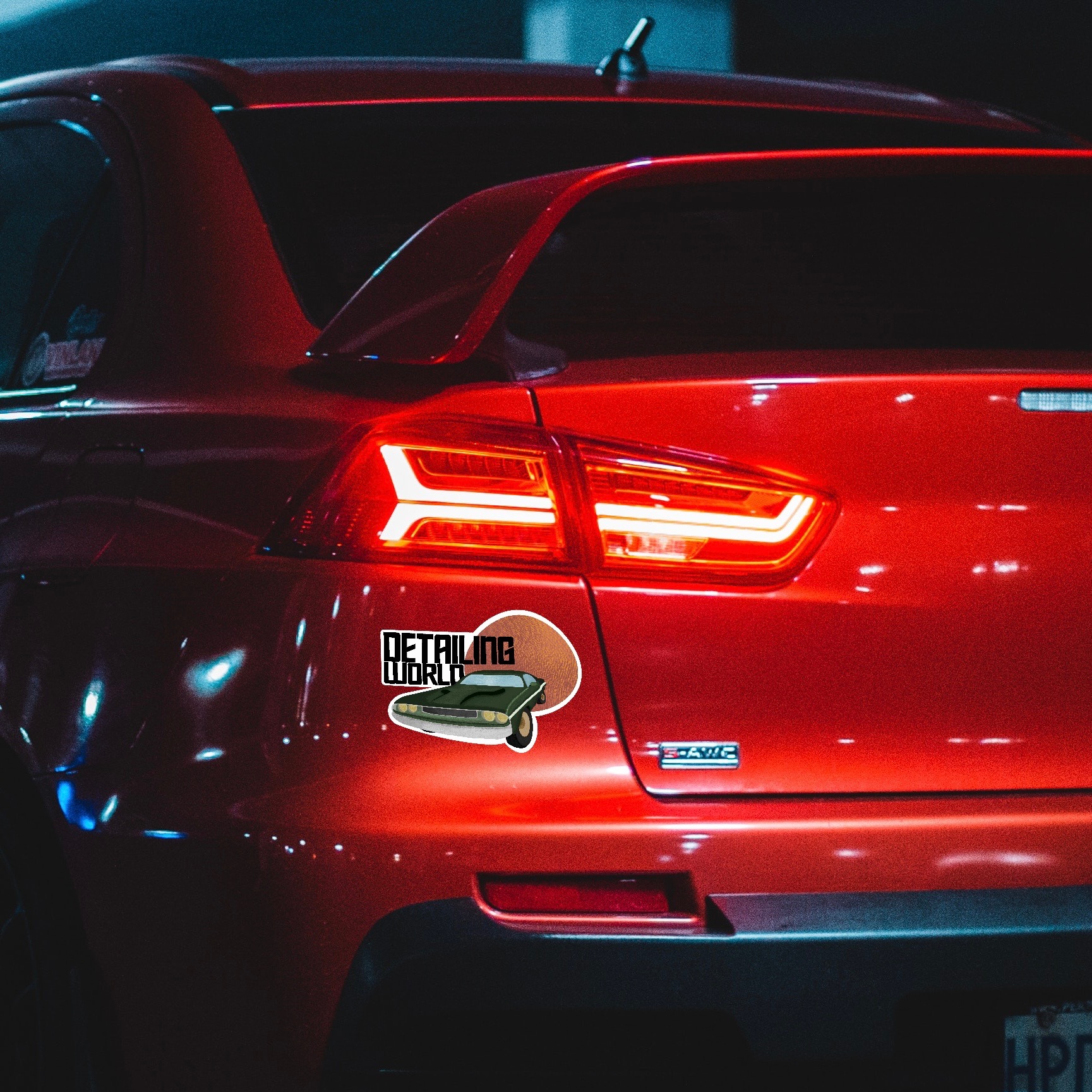 Czerwony samochód z naklejką 'Detailing World' przedstawiającą klasyczny model auta na tle tekstury skóry.
