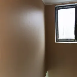 Wnętrze po nałożeniu gładzi w odcieniach beżu, widoczne okno z czarną ramą i fragment sufitu.