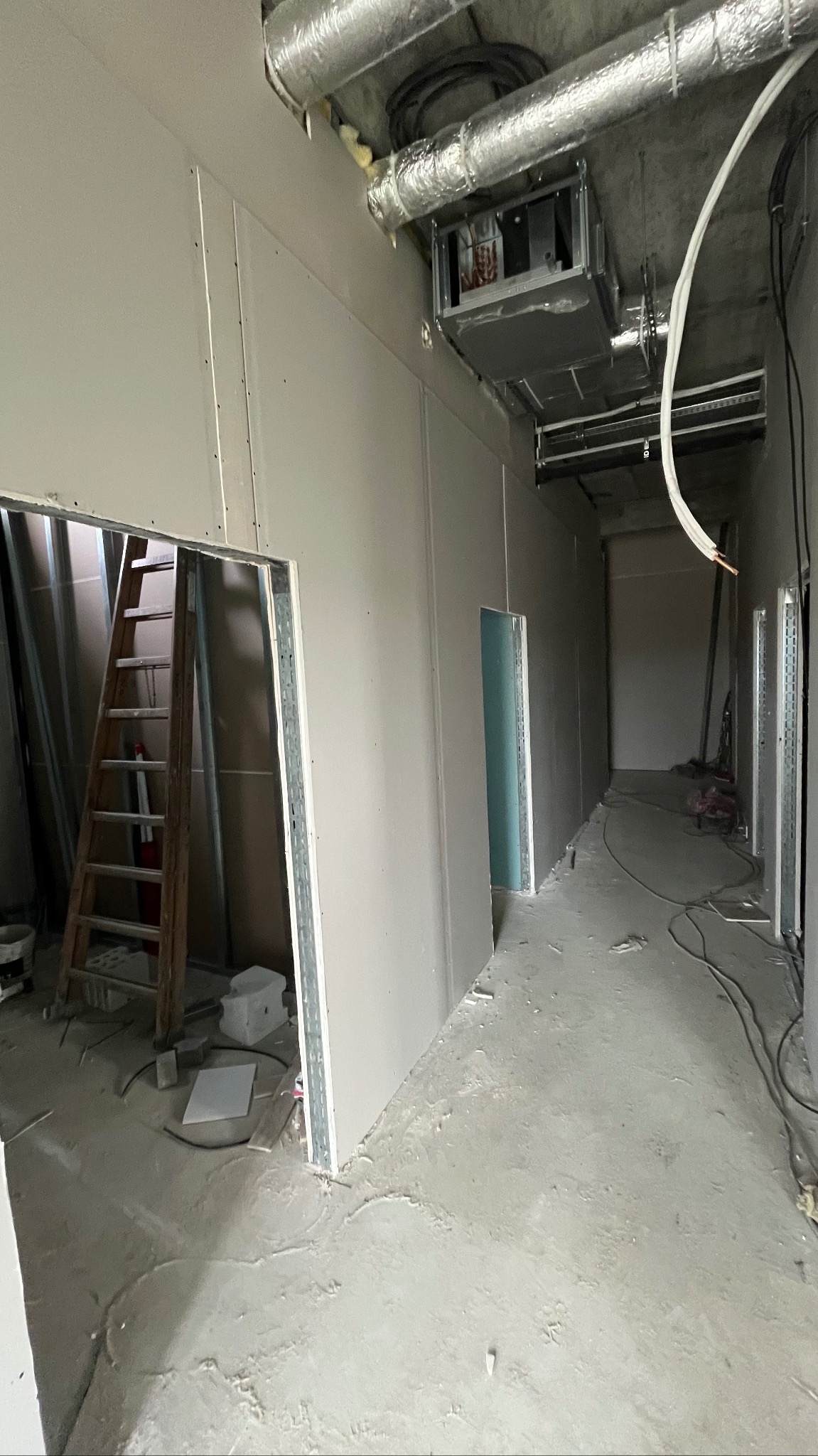 Korytarz w trakcie montażu płyt gipsowo-kartonowych, widoczne profile, drabina i instalacje pod sufitem. Surowy stan wykończenia, przygotowanie do dalszych prac.