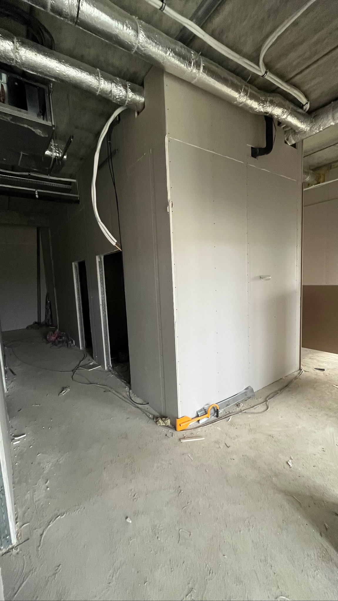 Montaż ścian działowych z płyt gipsowo-kartonowych w surowym wnętrzu. Widoczne narzędzia pracy i instalacje pod sufitem. Stan surowy, przed wykończeniem.