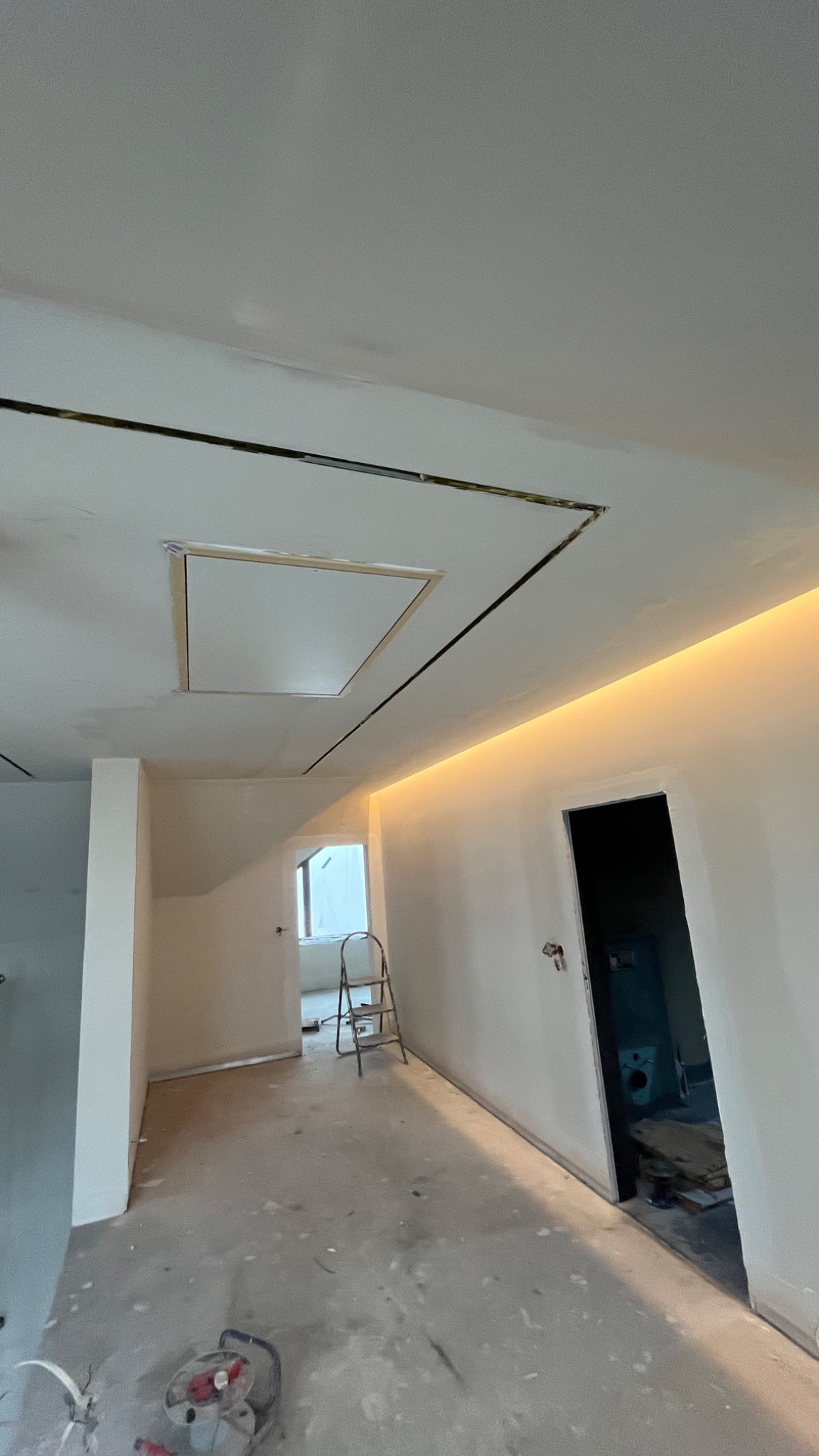Wykończony sufit podwieszany z oświetleniem LED i otworem rewizyjnym. Widoczna drabina i narzędzia na podłodze, sugerujące trwające prace wykończeniowe.