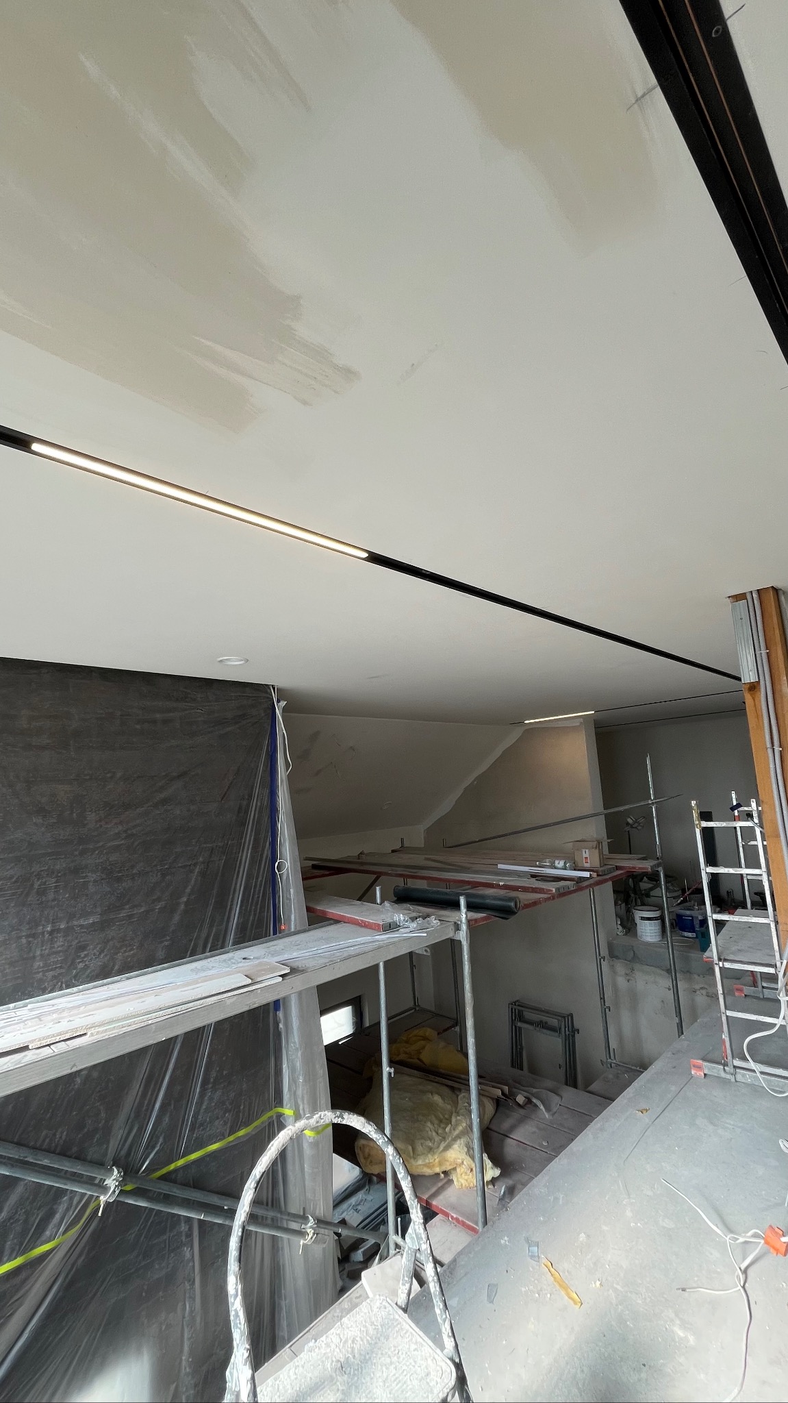 Sufit po szpachlowaniu i wstępnym malowaniu, widoczne rusztowania i przygotowania do dalszych prac wykończeniowych. Zamontowane oświetlenie liniowe.