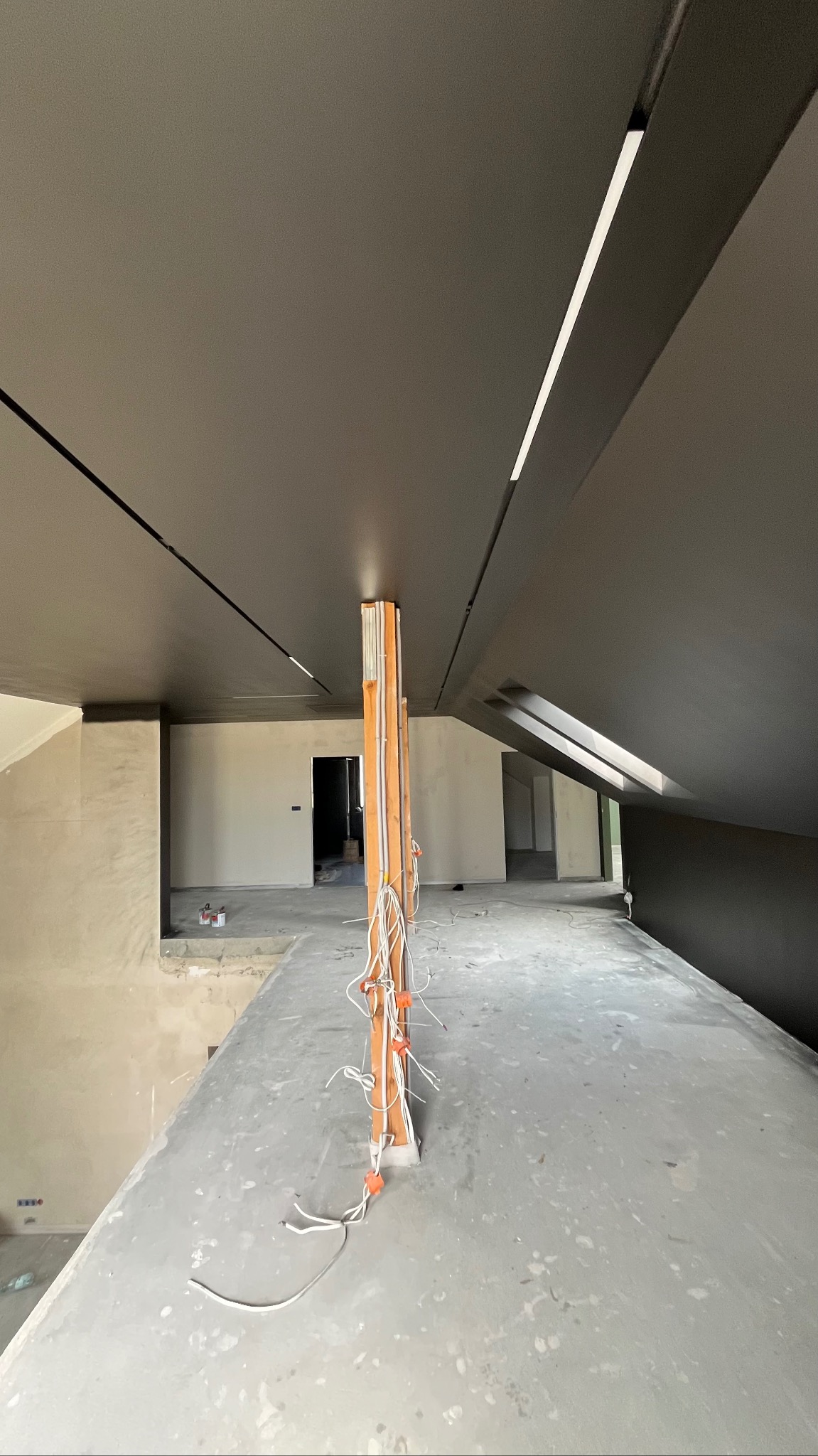 Wnętrze w trakcie prac wykończeniowych: szpachlowana ściana, podwieszany sufit z oświetleniem liniowym, widoczne przewody elektryczne. Surowy stan, przygotowanie do dalszych prac.