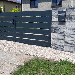 SIATKO-MET PAWEŁ ŚNIEŻEK - Nowoczesna, pozioma brama wjazdowa w kolorze antracytu, zintegrowana z murem z szarej kostki łupanej. Skrzynka na listy z numerem domu.