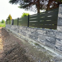 SIATKO-MET PAWEŁ ŚNIEŻEK - Nowoczesne ogrodzenie: poziome, zielone panele na murku z szarej kostki. W tle drzewa iglaste i trawa. Widok z poziomu gruntu, częściowo ukończony teren.