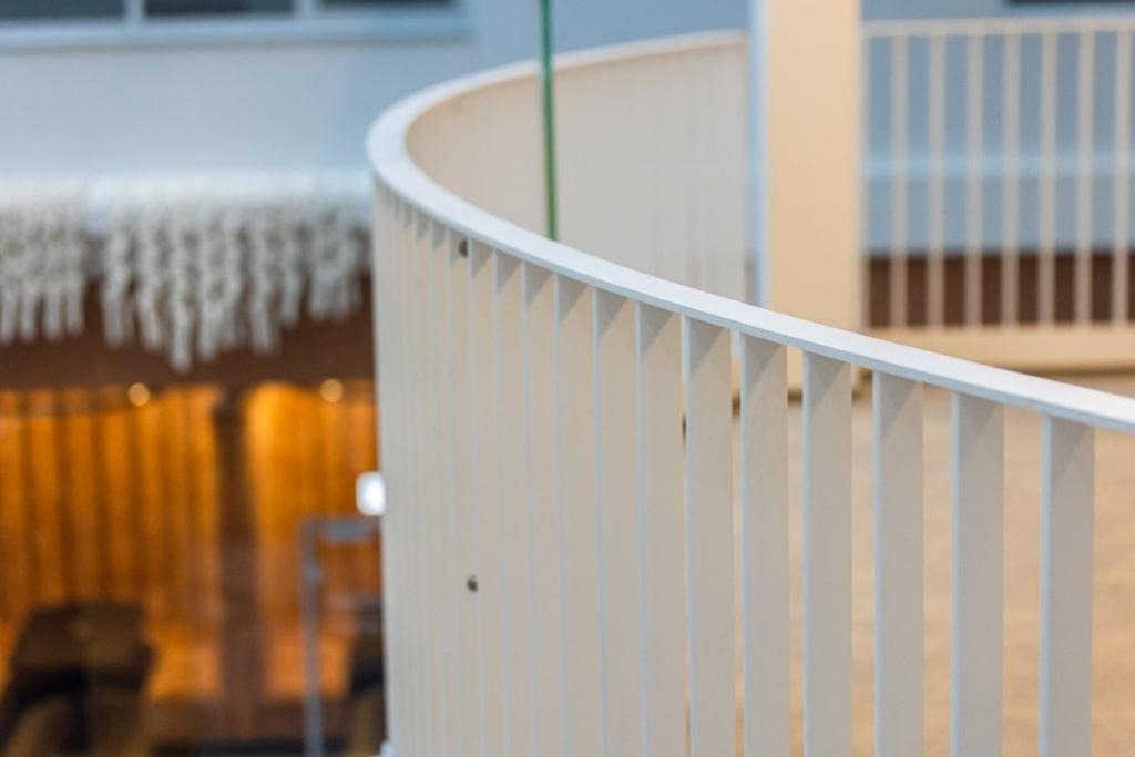 Biała, minimalistyczna poręcz schodowa z pionowymi szczebelkami, zakrzywiona linia, widok z góry, w tle elementy wystroju wnętrza.