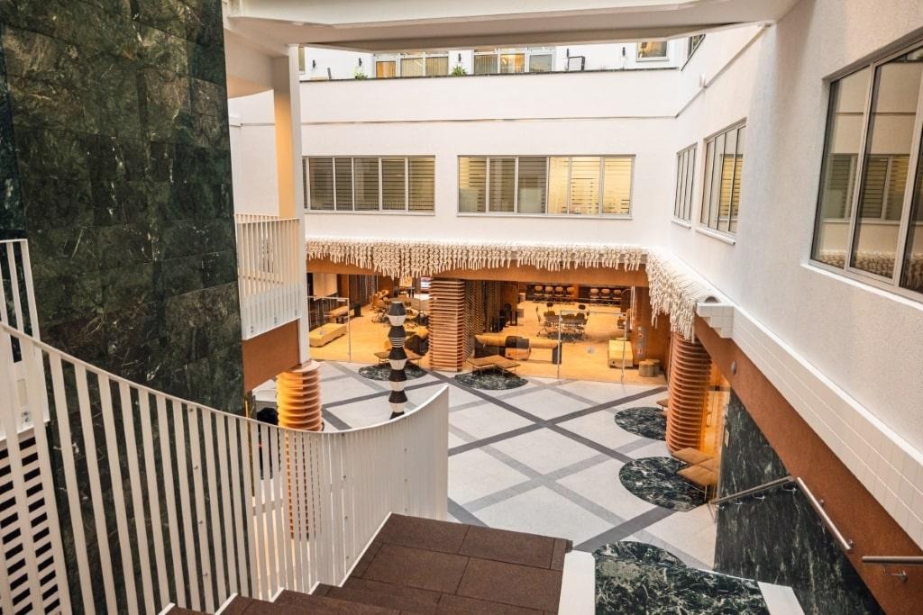 Wnętrze budynku biurowego z widokiem na hol z balustrady schodów, marmurowa ściana i kolumny, wykończenia w kolorze terakoty, szklane ściany biur w tle.