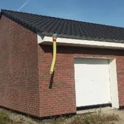 Nowo wybudowany budynek z czerwonej cegły z białą bramą garażową i drzwiami wejściowymi, widoczny pracownik z samochodem dostawczym w tle.