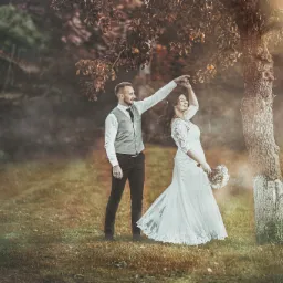 Para młoda tańczy pod drzewem z owocami w jesiennej scenerii, w tle widoczny domek na drzewie.