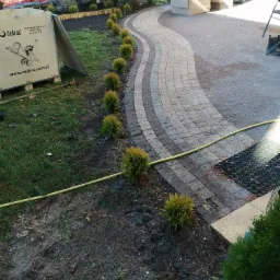 Kręta ścieżka z kostki brukowej w ogrodzie, obrzeża z małych, okrągłych krzewów, w tle skrzynia z rozdrabniaczem CEDRUS R802.