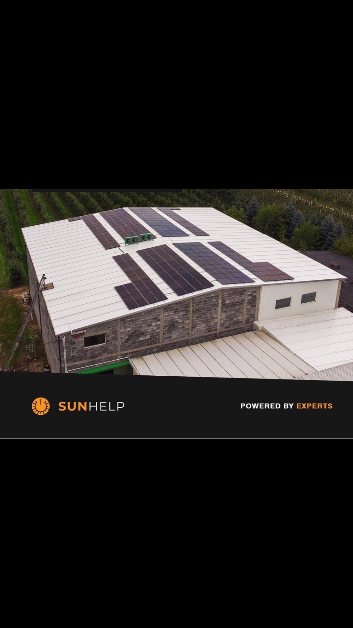 Instalacja paneli słonecznych na dachu budynku przemysłowego, widok z góry, otoczenie drzewa owocowe.