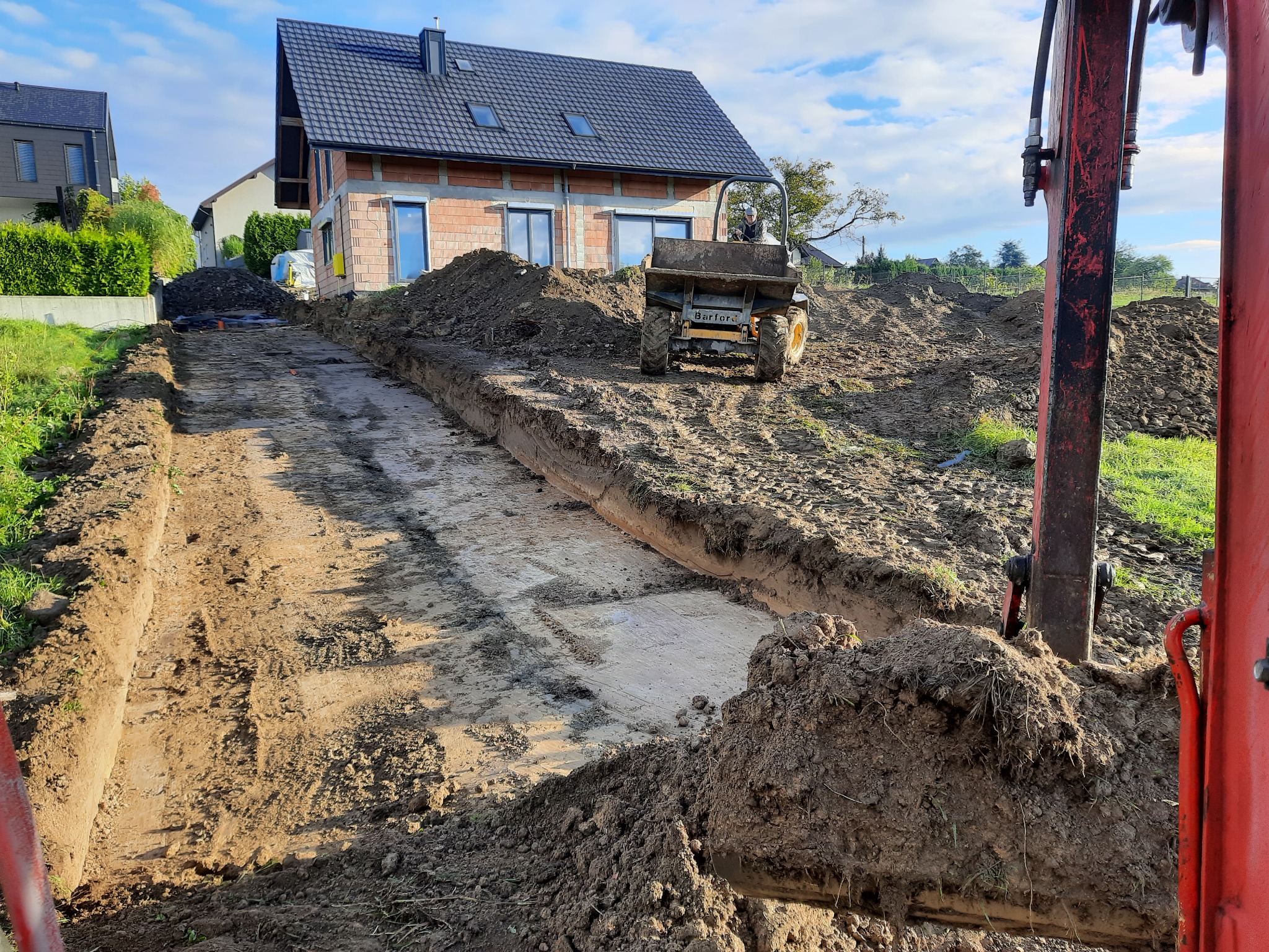 Wykop pod fundamenty domu jednorodzinnego w trakcie realizacji, widoczny mini dumper Barford na wyrobisku, oraz ramię koparki z przodu kadru.