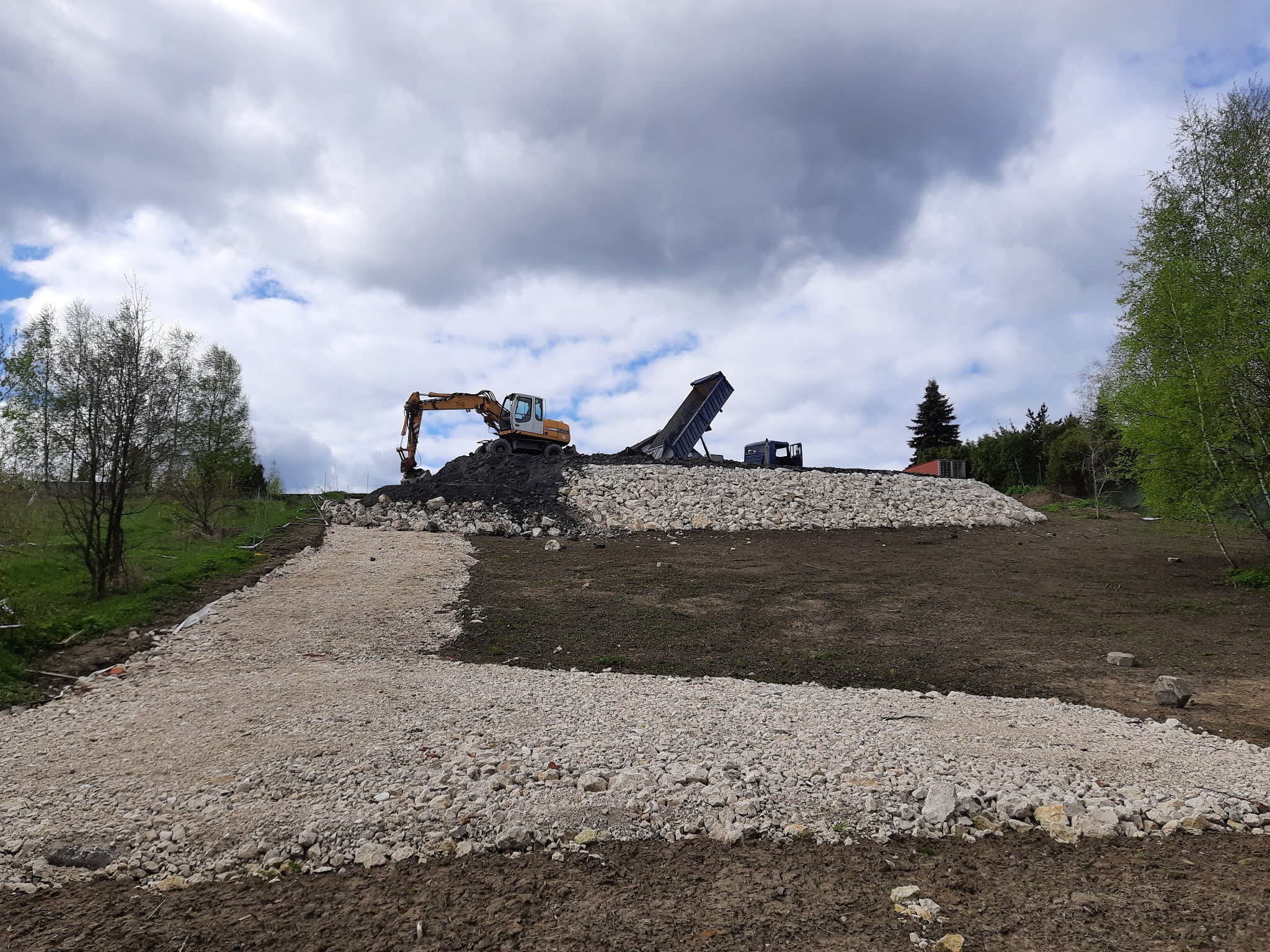 Spytkowice: Żwirowa droga w trakcie utwardzania, z koparką i wywrotką pracującymi na wzgórzu w tle, pod pochmurnym niebem.